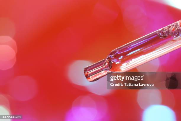 glass pipette with transparent face serum on purple red blurred background. beauty, cosmetic products, wellness, skin and body care concept - clear skin red background stock-fotos und bilder