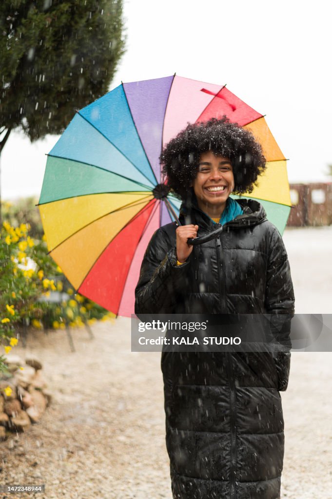 Portrait of young woman with afro hair under a multicolored umbrella on a snowy winter day