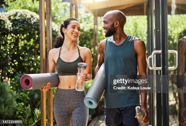 fitness, yoga personas caminando a clase con equipo de entrenamiento y botella de agua para el trabajo en equipo deportivo en el centro de bienestar. pilates, entrenamiento y pareja de amigos sanos hablando de ejercicio holístico en la naturaleza - gym couple fotografías e imágenes de stock