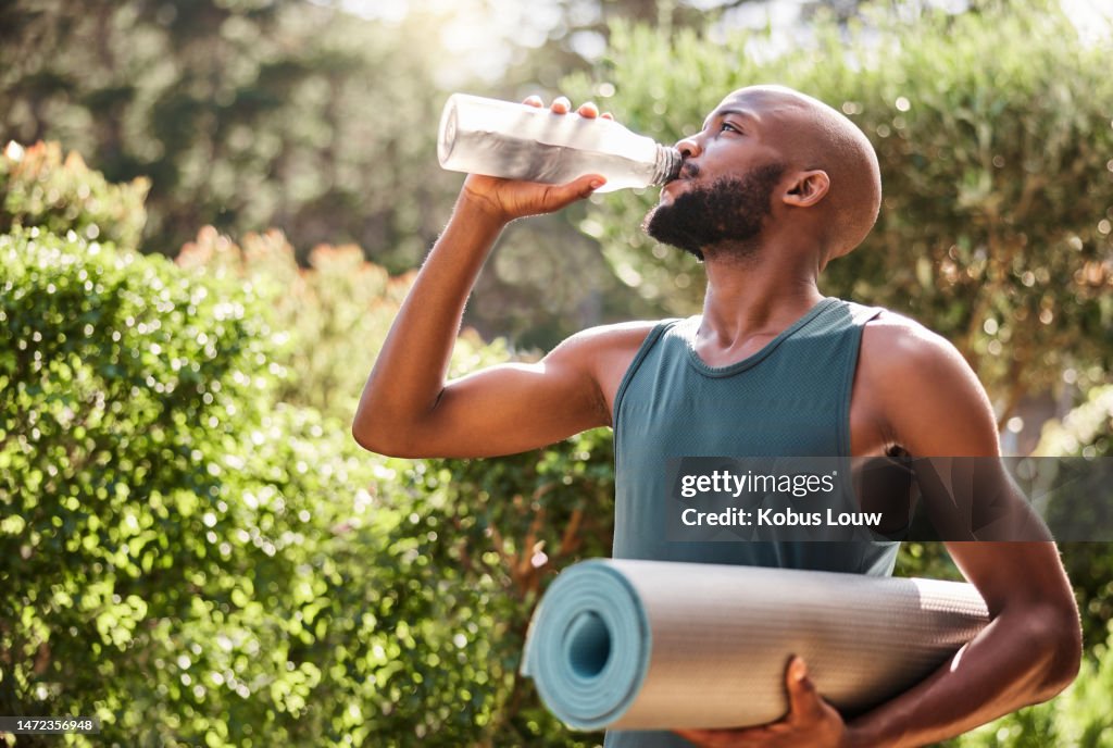 Yoga mat, fitness and black man drinking water in nature for health and wellness outdoors. Athlete, pilates and male yogi drink liquid for hydration after exercising, workout or training exercise.