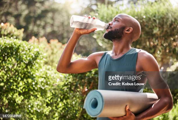 yoga mat, fitness and black man drinking water in nature for health and wellness outdoors. athlete, pilates and male yogi drink liquid for hydration after exercising, workout or training exercise. - wellbeing man stock pictures, royalty-free photos & images