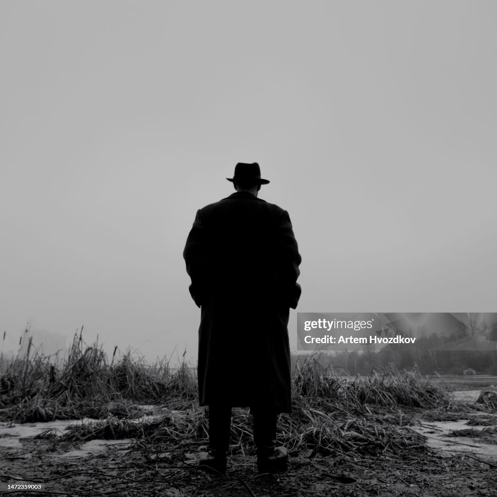 Silhouette of gangster standing at winter river swamp
