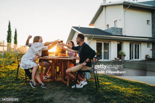 freunde stoßen bei sonnenuntergang gemeinsam mit rotwein an - vorgarten stock-fotos und bilder