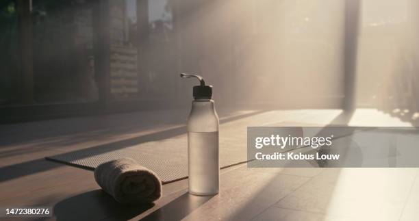 water bottle, towel and exercise mat in wellness studio or gym floor for yoga, fitness and training. healthy lifestyle, diet and mockup space with lens flare for advertising health club subscription - yoga studio stock pictures, royalty-free photos & images
