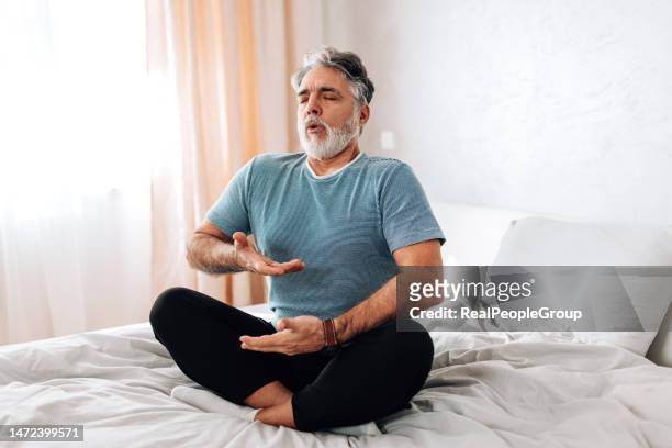 yoga in bed. this man shows how to create a peaceful morning routine - respirar imagens e fotografias de stock