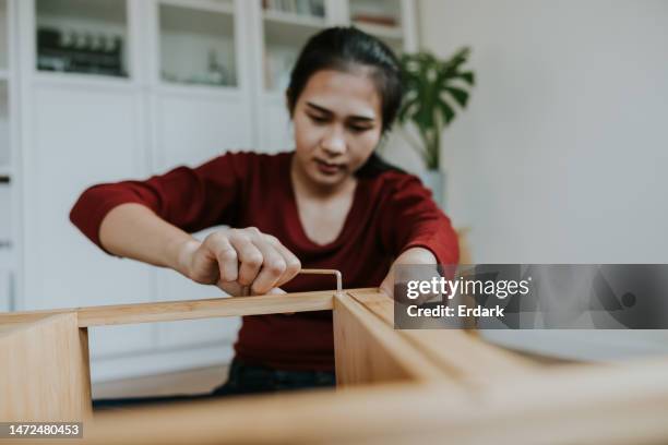 young woman with hand disability installing a wooden shelf by herself. - woman wrench stock pictures, royalty-free photos & images