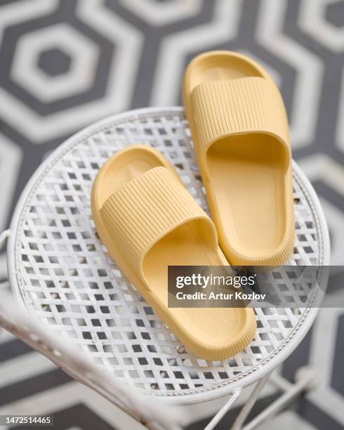 pair of women's slippers for shower or beach in beige. pair of house shoes on white mesh chair. rubber slippers. against background of gray and white tiles. soft focus. top view. copy space - plastic pool stock-fotos und bilder