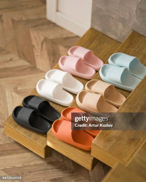 set of house slippers for whole family. six pairs of colorful slippers in row on steps of wooden staircase. rubber shoes. shower slippers. men's and women's slippers. top view. soft focus. copy space - paio foto e immagini stock