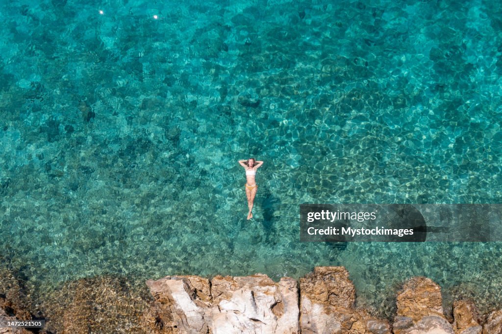 Woman floating on turquoise sea, she enjoys her summer vacations, sun shining and clear water