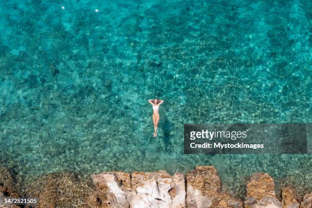 woman floating on turquoise sea, she enjoys her summer vacations, sun shining and clear water - croatia coast imagens e fotografias de stock