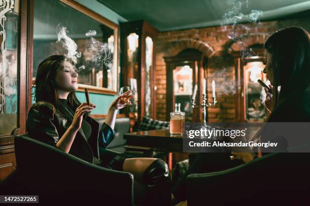 mujer disfrutando de la compañía del otro mientras bebe ron y fuma cigarros - beautiful women smoking cigars fotografías e imágenes de stock