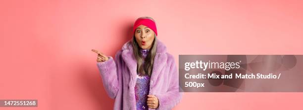 cool asian granny pointing finger right and showing promo offer - glamourous granny stockfoto's en -beelden