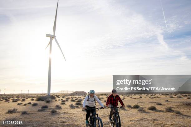 e-mountain bikers ride through desert below wind turbine - wind fahrrad stock-fotos und bilder