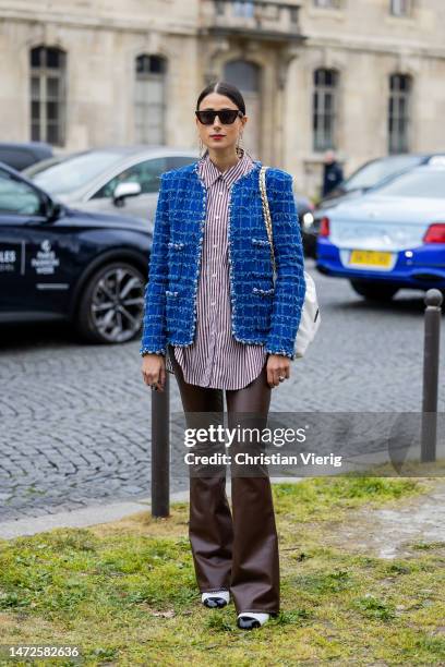 Julia Haghjoo wears striped button shirt, blue jacket, brown leather flared pants, white bag, white black shoes, sunglasses, earrings outside Chanel...