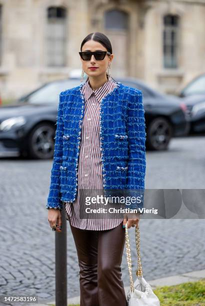Julia Haghjoo wears striped button shirt, blue jacket, brown leather flared pants, white bag, white black shoes, sunglasses, earrings outside Chanel...