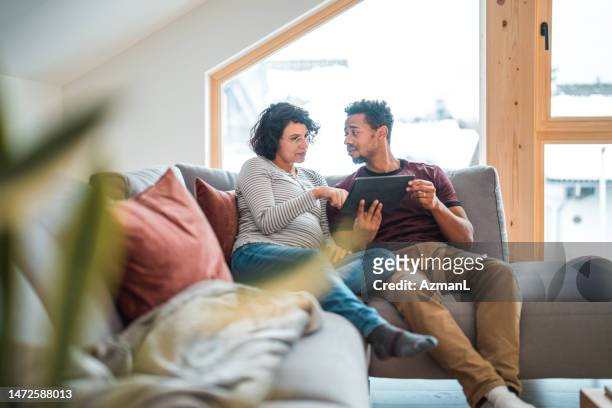 mixed race pregnant couple buying baby clothes online with a digital tablet - tablet couple stock pictures, royalty-free photos & images