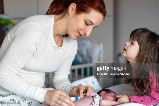 mutter entfernt die gaze von der nabelschnur des neugeborenen. die ältere schwester schaut zu und hilft. - umbilical cord stock-fotos und bilder