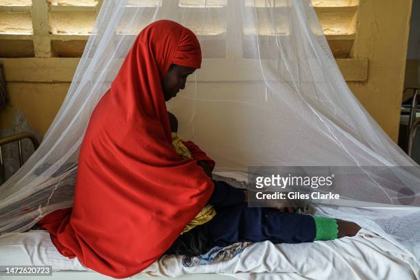 Zaynab, aged 25, sits on a hospital bed at Trocaire Referral Health Center behind a mosquito net, holding her sick one-year-old, Omar on October...