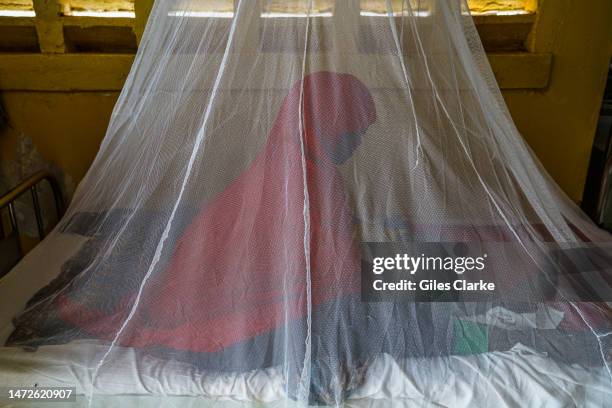 Zaynab, aged 25, sits on a hospital bed at Trocaire Referral Health Center behind a mosquito net, holding her sick one-year-old, Omar on October...