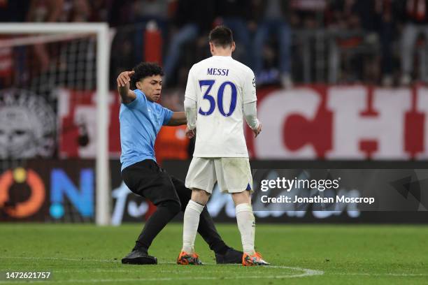 Lionel Messi of PSG looks on as pitch invader slides by following the final whistle of the UEFA Champions League round of 16 leg two match between FC...