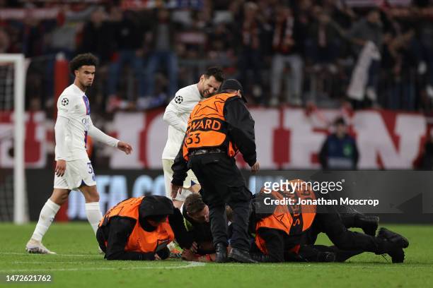 Lionel Messi grimaces as a steward slides into the back of him attempting to stop a pitch invader during the UEFA Champions League round of 16 leg...