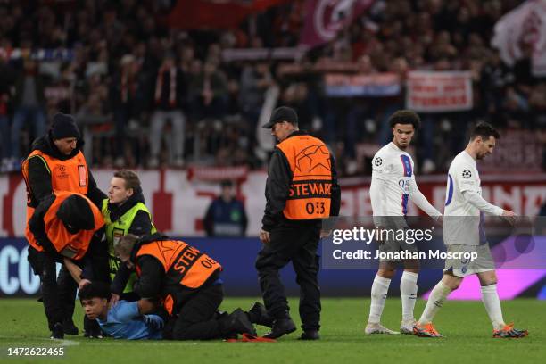 Warren Zaire-Emery and Lionel Messi of PSG leave the field of play as stewards deal with a pitch invader following the final whistle of the UEFA...