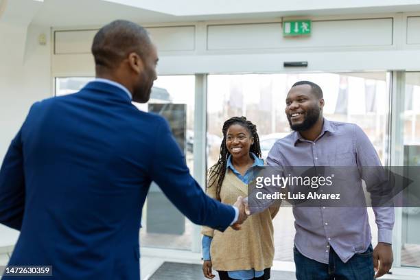 salesman welcoming a couple with a handshake in car showroom - sliding door - fotografias e filmes do acervo