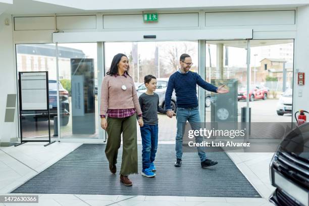 family of three looking at a new car model to buy in a dealership - show room photos et images de collection