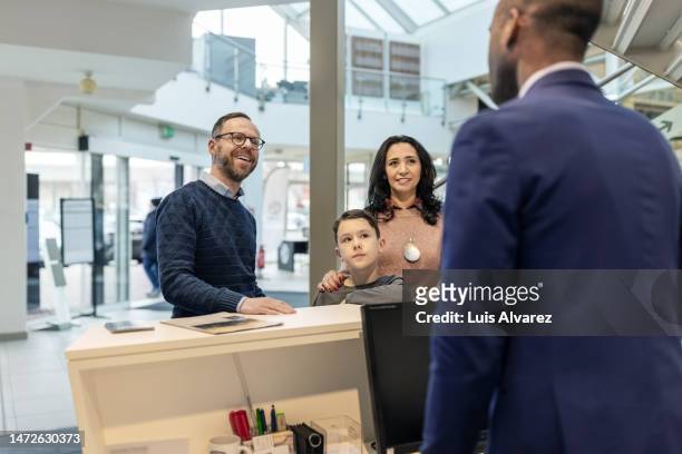 family visiting car showroom talking with salesman at front desk - car rental stock pictures, royalty-free photos & images