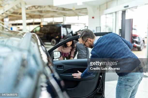 mature man checking the new car interior with family at car showroom - car rental stockfoto's en -beelden