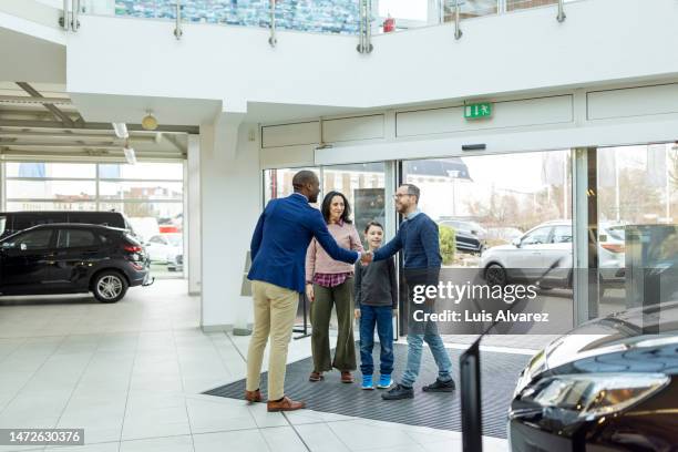 automobile dealer shaking hands with family visiting a car showroom - autodealer stockfoto's en -beelden