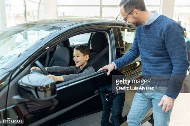 father and son choosing a new car to buy at automobile dealership - family inside car fotografías e imágenes de stock