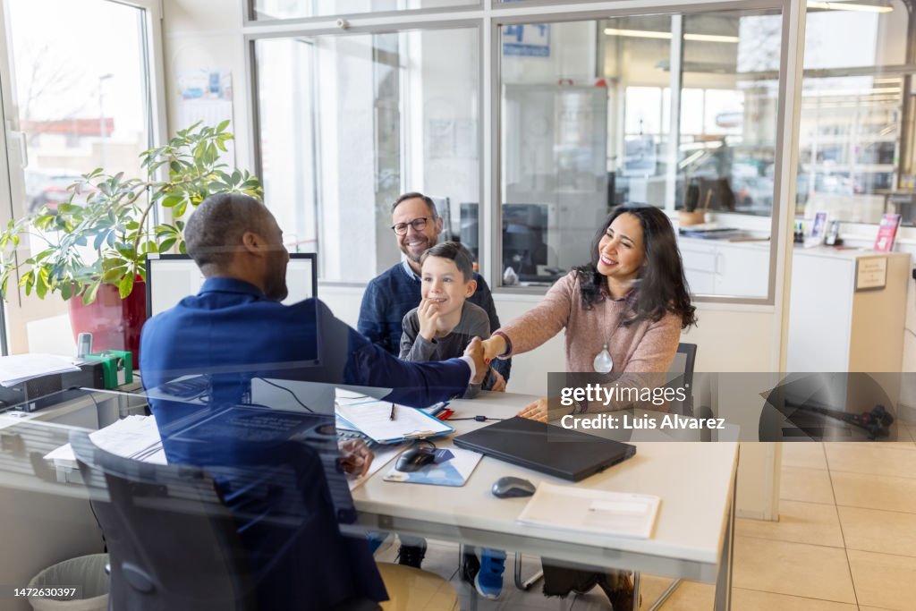 Car salesman shaking hands with family sitting in his office at showroom
