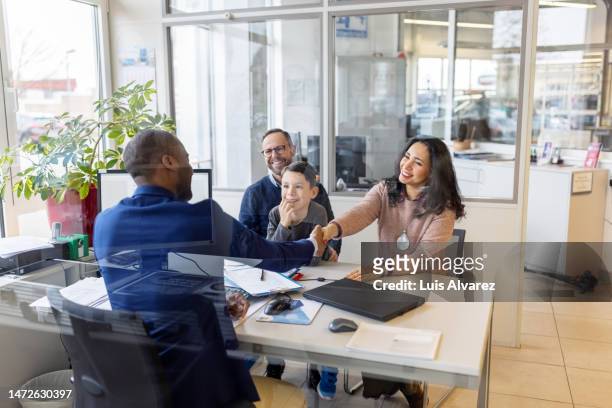 car salesman shaking hands with family sitting in his office at showroom - generation contract stock pictures, royalty-free photos & images
