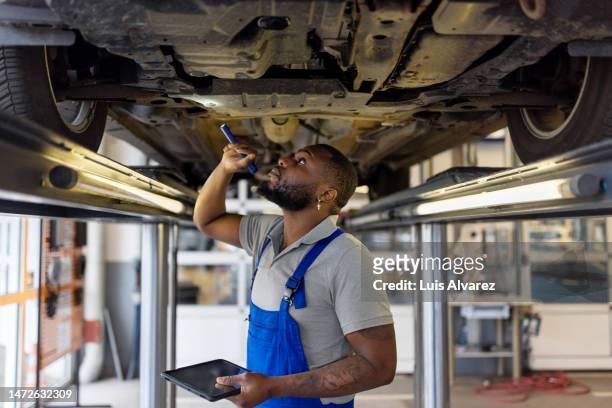 auto repair specialist examining brake pads of lifted car during inspection - car repair stockfoto's en -beelden