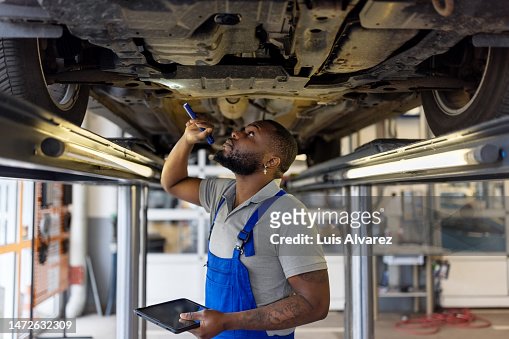 Auto repair specialist examining brake pads of lifted car during inspection