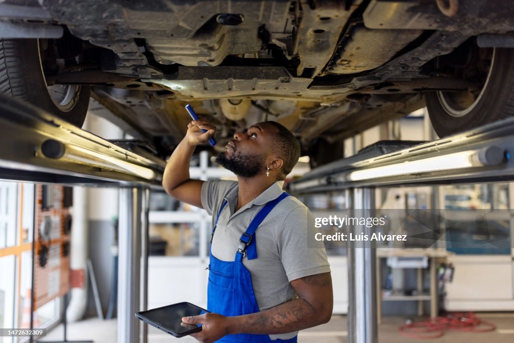 Auto repair specialist examining brake pads of lifted car during inspection