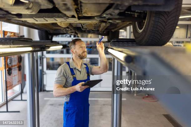 repair man inspecting the vehicle before maintenance at service station - meccanismi foto e immagini stock