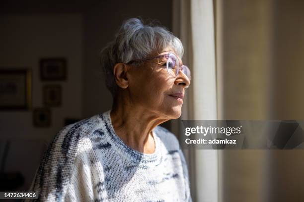 senior woman looking out the windows of her home - verlaten stockfoto's en -beelden