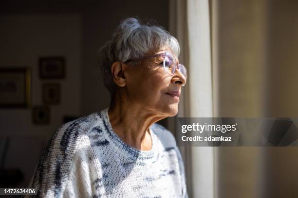 senior woman looking out the windows of her home - japanese old woman stock pictures, royalty-free photos & images