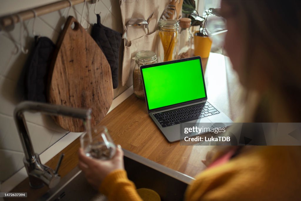 While working at home, female freelancer uses her laptop and pours a glass of water to refresh herself