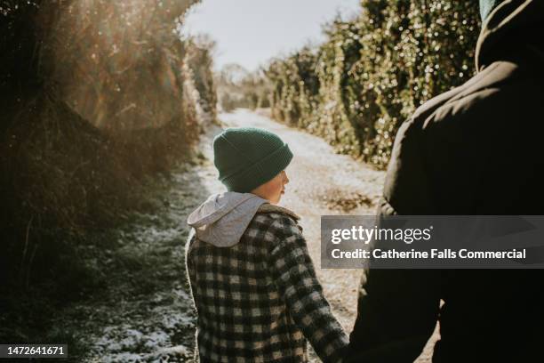 a little boy has a quiet moment on a snowy path, walking beside his father, holding hands - family wellbeing stock pictures, royalty-free photos & images