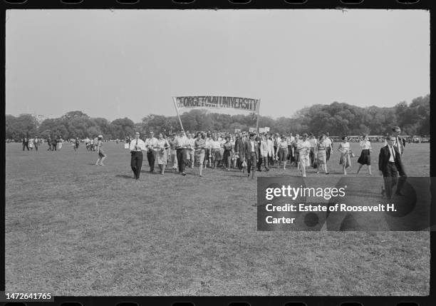 View of Civil Rights demonstrators, some carrying a large 'Georgetown University' banner, as they walk on the grass during the March on Washington...