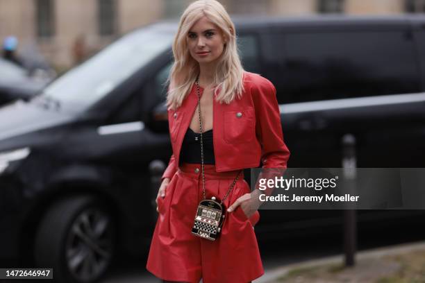 Xenia Adonts seen wearing a red leather set with a jacket and shorts, a black top, black transparent tights, black loaders and a jukebox bag before...
