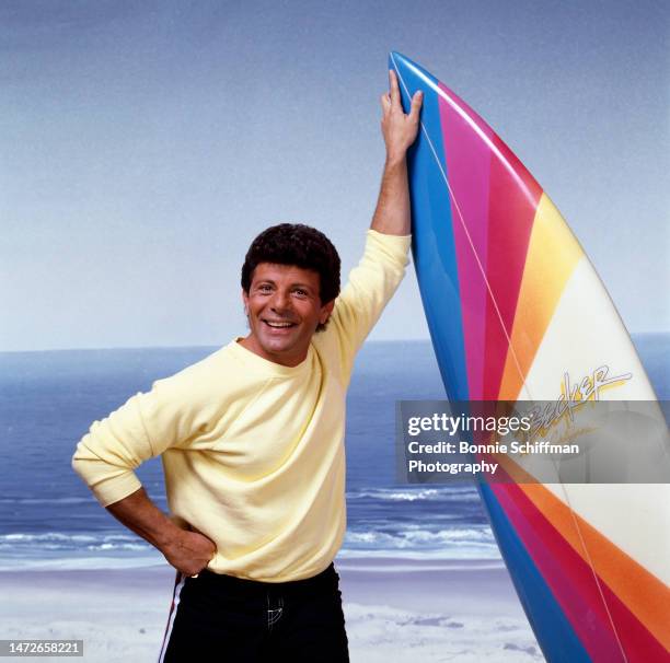 Actor and musician Frankie Avalon stands with his hand on his hip and his other hand holding up a colorful surfboard in Los Angeles in 1987.