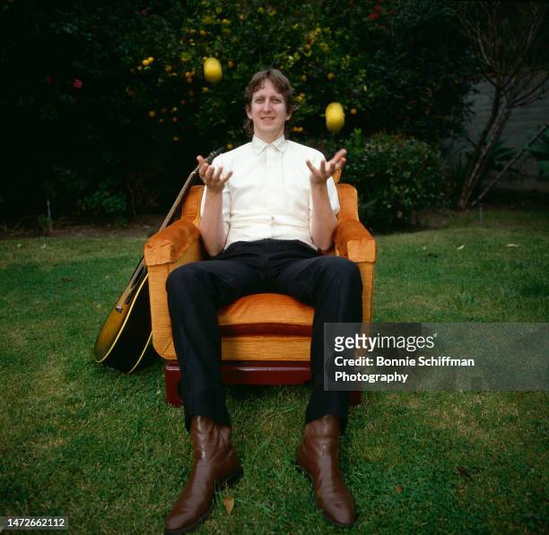 Musician T-Bone Burnett juggles lemons while seated in a plush orange velvet chair flanked by his guitar outside in Los Angeles in 1982.