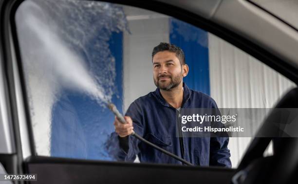 man working at the car wash cleaning a window with a high-pressure hose - car wash stock pictures, royalty-free photos & images