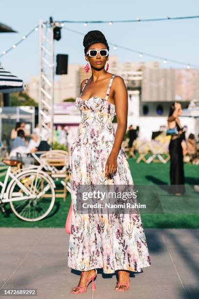 Guest is seen wearing an floral maxi dress, white sunglasses, pink shoes and pink handbag outside the Suit Up Runway at Melbourne Fashion Festival on...