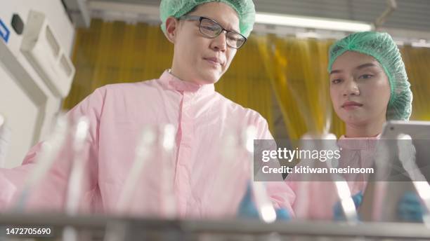 nutritionist or quality control or food scientist worker, wearing hairnet and sterile clothing, discussing while checking quality control of product of machine filling fruit juices into bottles on tablet. employee work in bottled fruit juice factory. - chief scientist stock pictures, royalty-free photos & images