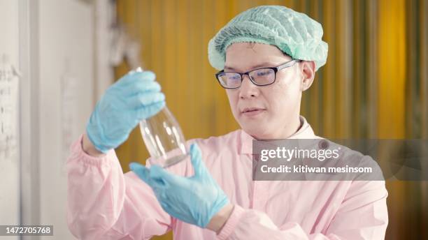 male manager factor or engineers or chief leader of production line wearing hairnet and sterile clothing and gloves, walk through the yellow plastic dust curtain, checking quality control of product of machine filling fruit juices at manufacturing plant. - chief scientist stock pictures, royalty-free photos & images